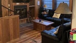 Un salon chaleureux avec des murs en bois, une cheminée, un téléviseur et un canapé.