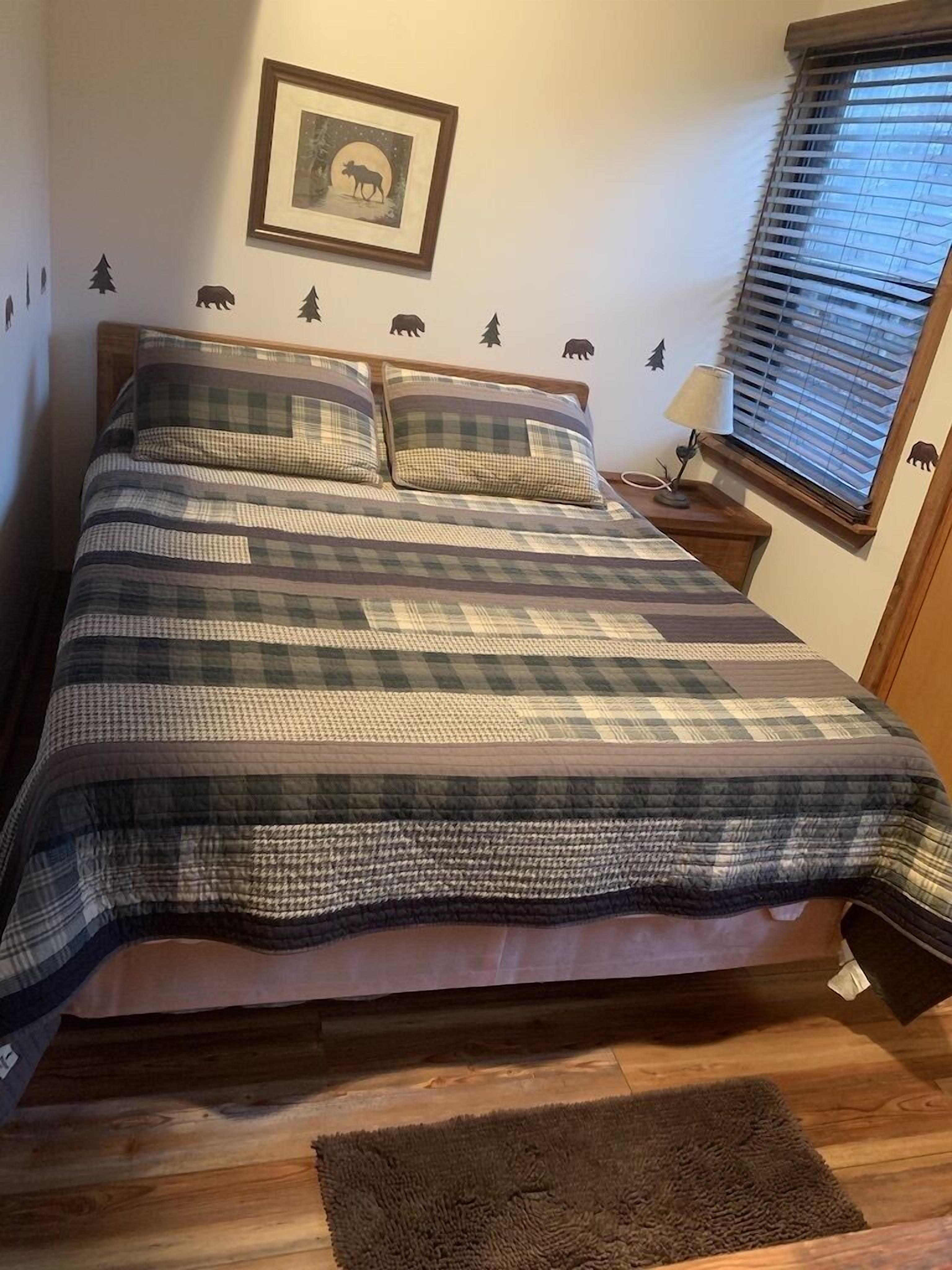 A bed with a plaid bedspread, a bedside lamp, and a framed picture on the wall.