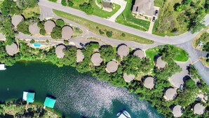 An aerial view of a lakeside property with a circular dock, a parking area, and a building with a sloped roof. - Lakefront Retreat with Pool & Hot Tub [#1 Ocotillo] (Lakeway)
