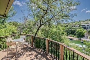 A wooden deck with a table and chairs, overlooking a river and greenery. - Ocotillo #1 - Lakefront Retreat with Pool & Hot Tub (Lakeway)