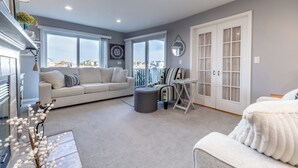 A spacious living area with a sofa, ottoman, and a striped chair. There are large windows offering a view of the city. - 2027 OPEN! Lake Views New Buffalo Condo w/ Association Pool! (New Buffalo)