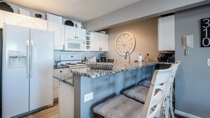 A modern kitchen with white cabinetry, a built-in stove, and a granite countertop. There is a round wall clock and a phone on the wall. - 2027 OPEN! Lake Views New Buffalo Condo w/ Association Pool! (New Buffalo)