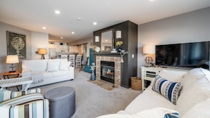 A modern living room with a fireplace, a television, and a dining area in the background. - 2027 OPEN! Lake Views New Buffalo Condo w/ Association Pool! (New Buffalo)