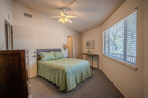 A bedroom with a bed, a ceiling fan, a window with blinds, and a small table with a lamp. - Texas Thistle #9 - Waterside Villa with Spa Amenities (Lakeway)