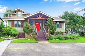 A two-story house with a red front door, a front porch, and a driveway leading to the entrance.