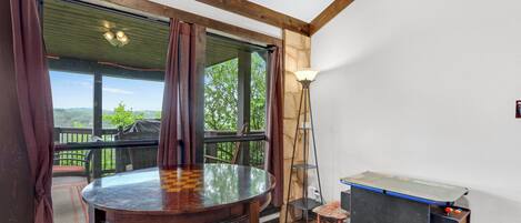 Una habitación con una mesa redonda, sillas, un taburete pequeño, una mesa de ping pong y vistas amplias a través de grandes ventanales.