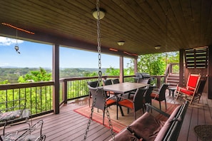 A covered outdoor deck with a table and chairs, a hanging light fixture, and a view of the landscape.