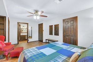 A bedroom with a bed, a red chair, a wooden door, and a ceiling fan.
