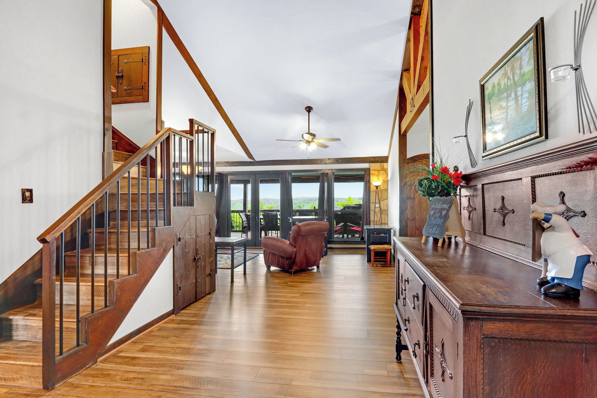 A spacious interior with a wooden staircase, a leather armchair, and a view through large windows.