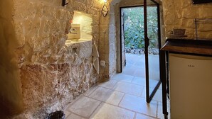 A rustic stone kitchen with a stone sink, a small refrigerator, and a view through an open doorway to a garden. - AMMARE BY THE SEA         (Marina di Novaglie)