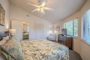 Ein Schlafzimmer mit Bett, Deckenventilator, Kommode, Fernseher und einem Fenster mit Jalousien.