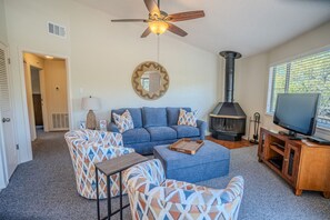 A living room with a sofa, ottoman, and patterned chairs, a television, a fireplace, and a ceiling fan. - Primrose #6 - Lake View Retreat with Hot Tub Access (Lakeway)