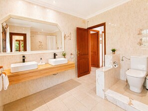 Un bagno moderno con due lavandini, uno specchio grande, un water e uno spazio doccia.