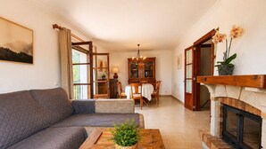 A living room with a sofa, a wooden coffee table with a plant, a fireplace, and a dining area with a table and chairs. - Can Pou - private pool - wifi - AACC (S'Aranjassa)