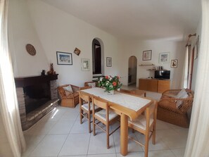 Uma sala de estar aconchegante com lareira, uma mesa de jantar com cadeiras, uma TV e uma área de cozinha.
