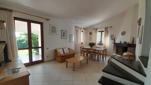 Una sala de estar amplia con chimenea, comedor y un gran ventanal corredizo que da a un jardín.