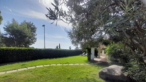 Un jardín bien cuidado con un camino pavimentado, setos cuidadosamente recortados y una gran roca.