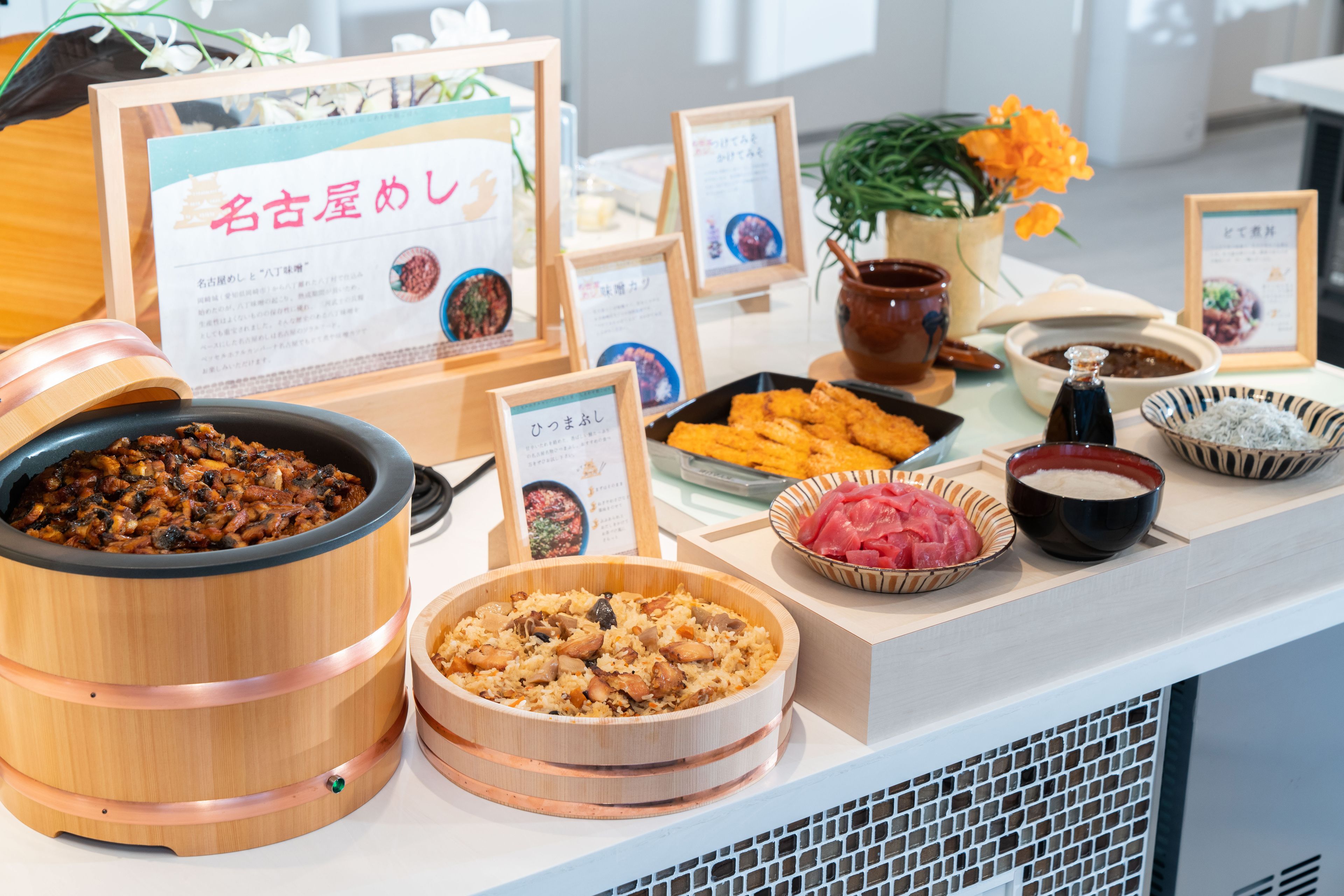A buffet table with various dishes, including a large wooden barrel, bowls of rice, and a bowl of sliced meat.