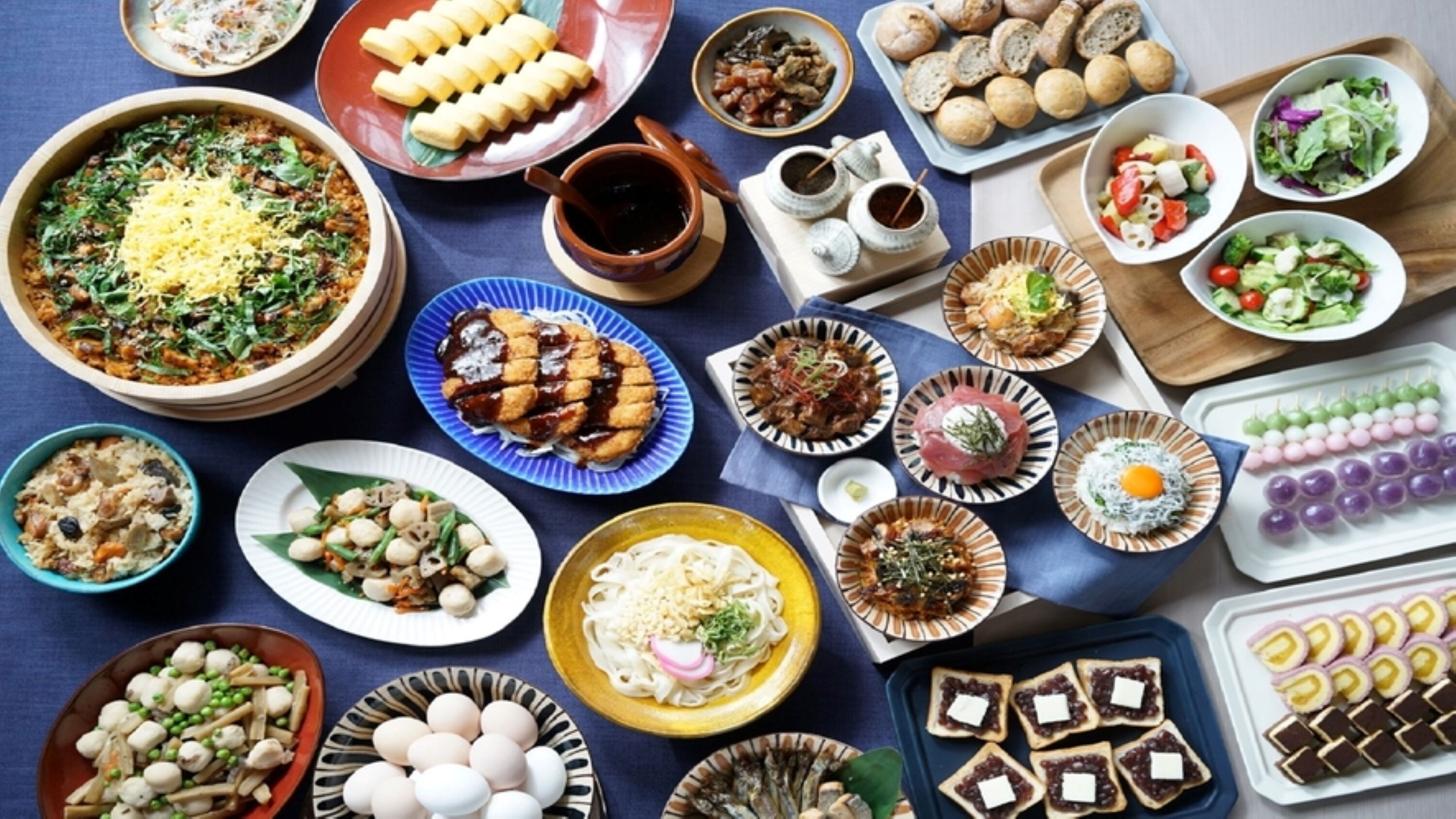 A variety of dishes arranged on a table, including sushi, pasta, and bread.
