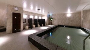 Een moderne badkamer met een groot zwembad, meerdere wastafels en een klok aan de muur.
