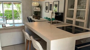 Una cocina moderna con una isla grande, taburetes de bar, horno empotrado y un armario con puerta de vidrio.
