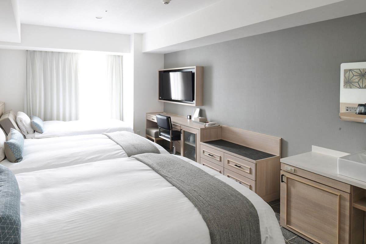 A hotel room with two beds, a desk, a TV, and a bathroom.