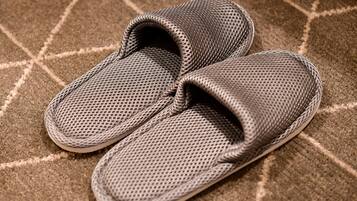 A pair of gray slippers with a textured surface, placed on a carpet with a geometric pattern.