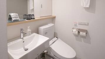 A modern bathroom with a white sink, toilet, and bidet. There is a mirror above the sink, a towel hanging on the wall, and a soap dispenser on the sink.