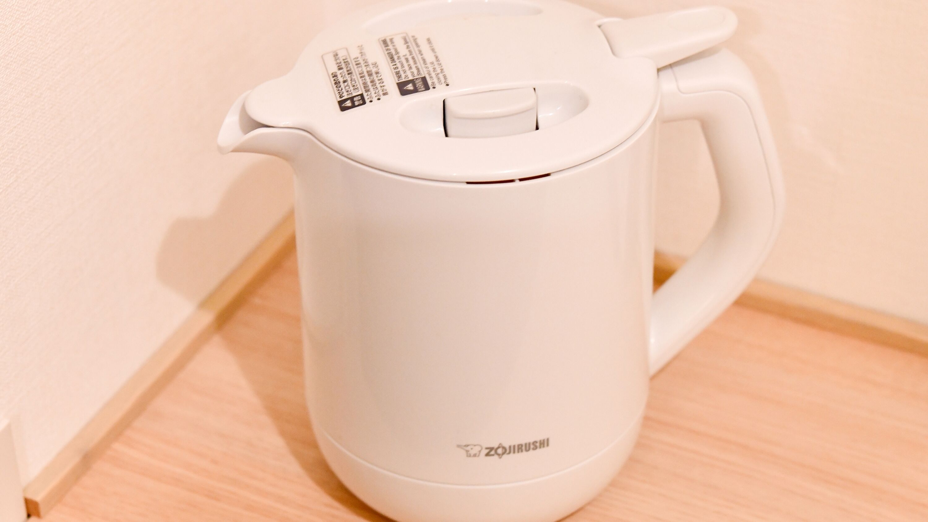 A white electric kettle with a handle and a spout, placed on a wooden surface.