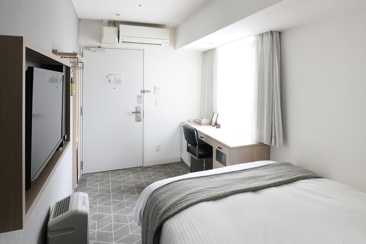 A hotel room with a bed, a desk, a television, and a window with curtains.