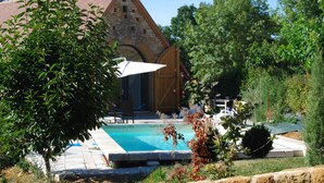 Ein Poolbereich mit einem dahinter liegenden Steinhaus, umgeben von Grün.