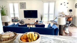 Una sala de estar con sofá, televisor, mesa de comedor y cesta de fruta.
