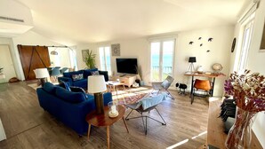 A living room with blue sofas, a TV, a coffee table, and a dining area with chairs.