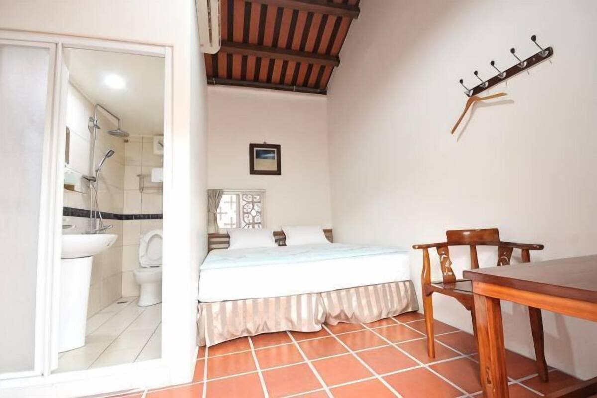 Un dormitorio con cama, una mesa de madera, una silla, ducha y un inodoro.