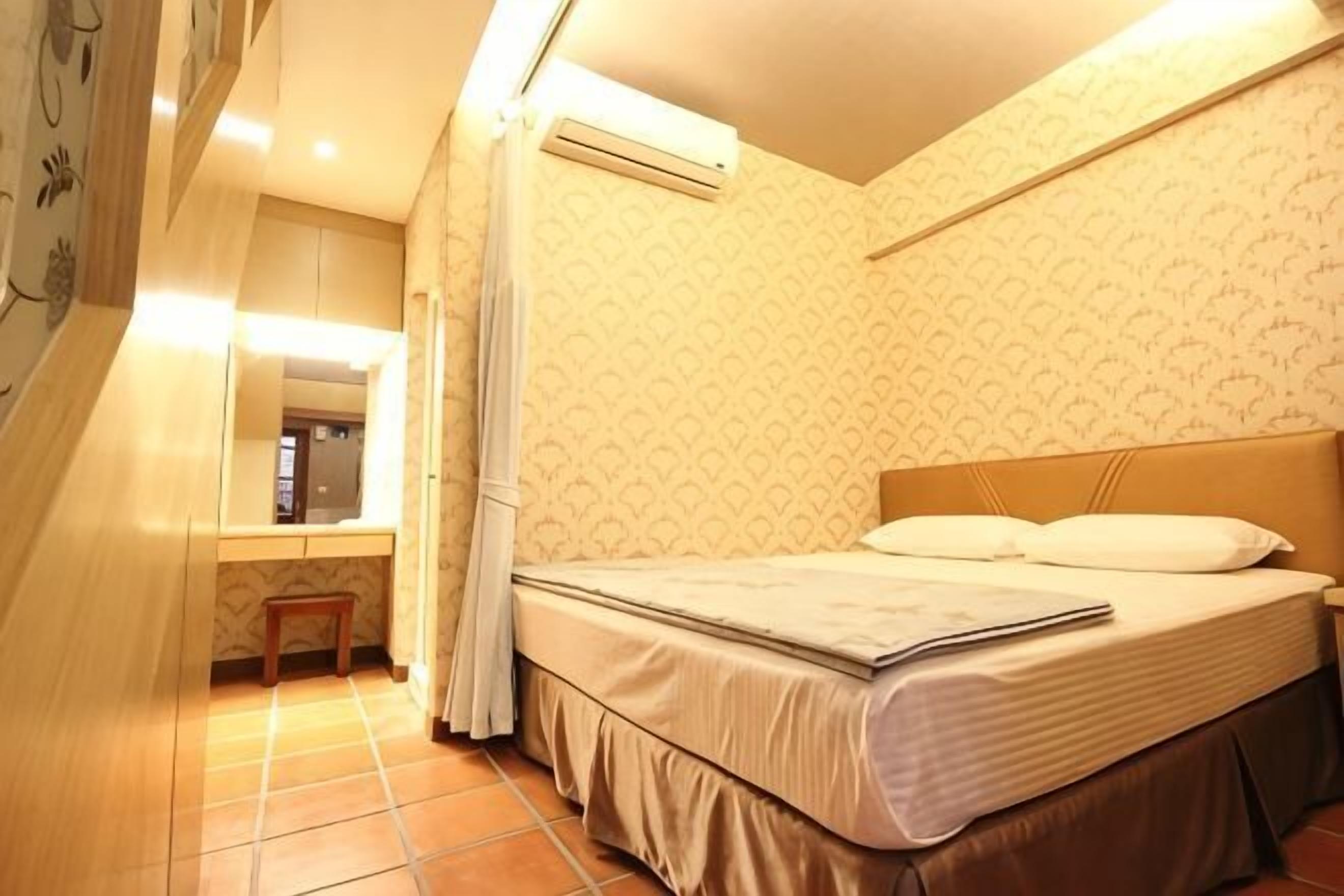 Un dormitorio con una cama, una mesita de noche, un espejo y un taburete pequeño.