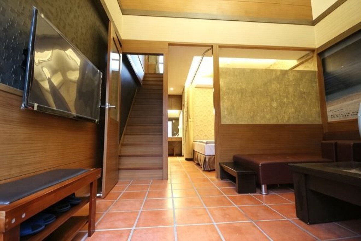 A hotel hallway with a wooden bench, a staircase, and a television mounted on the wall.