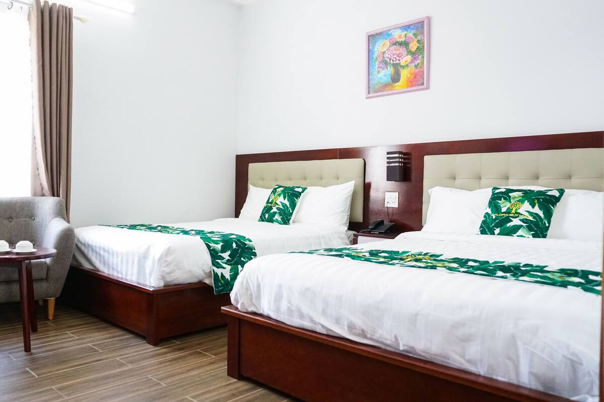 A hotel room with two beds, a chair, a small table, and a painting on the wall.
