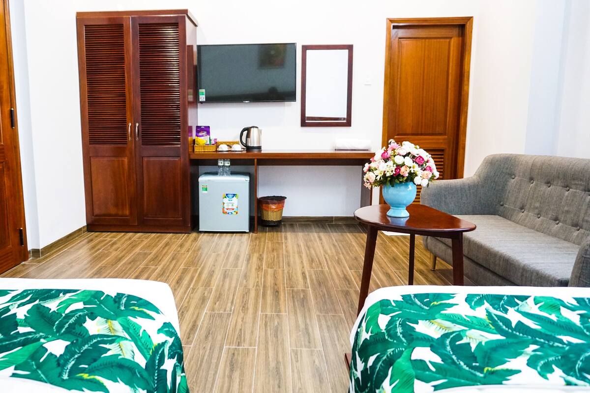 A hotel room with two beds, a desk with a computer, a TV, and a sofa.