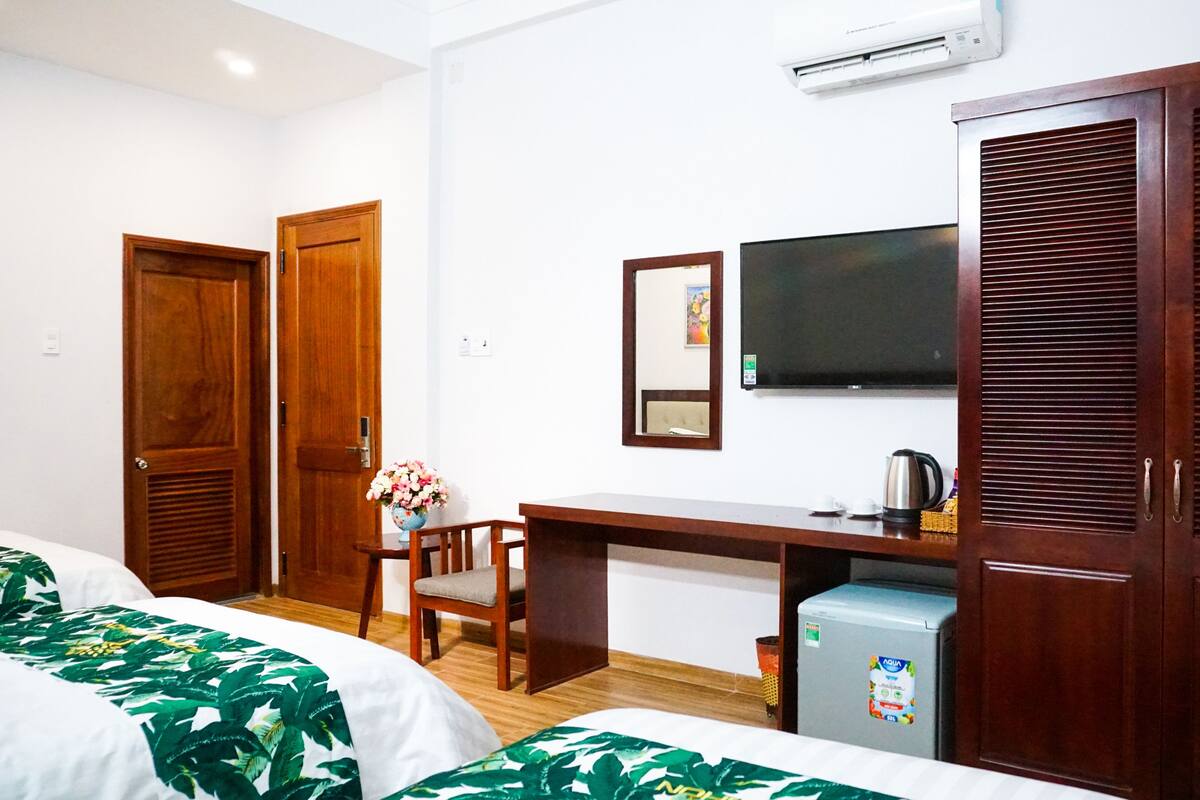 A hotel room with two beds, a wooden desk, a television, and a minibar.