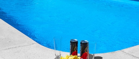 Zwembad met twee blikjes bier en een schaal chips op de rand.