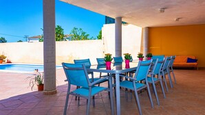 Une terrasse extérieure couverte avec une piscine, des chaises bleues et des murs orange.