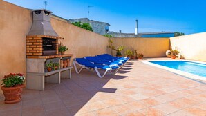 Une terrasse avec un barbecue, des fauteuils de jardin bleus, une piscine et des plantes en pot.