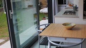 Une cuisine moderne avec une porte vitrée donnant sur un jardin, une table à manger avec des chaises et un four à micro-ondes.