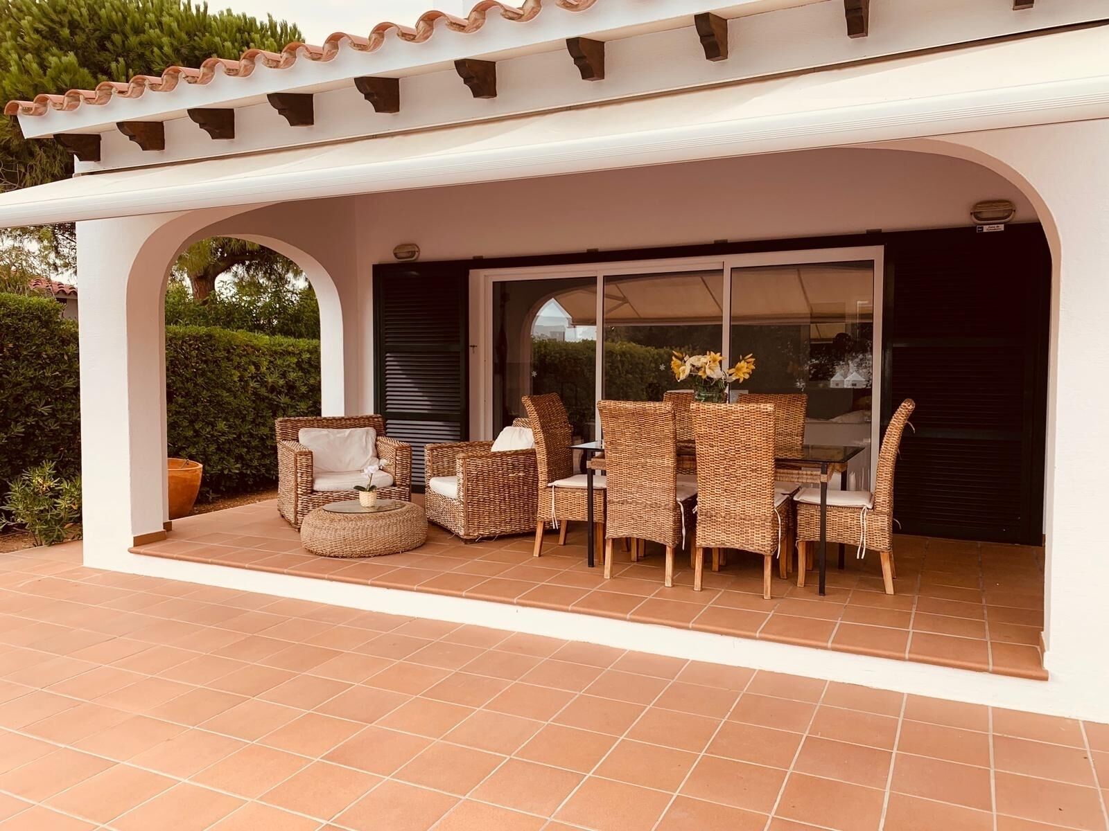 An outdoor patio area with wicker furniture, a glass door leading inside, and a tiled floor.