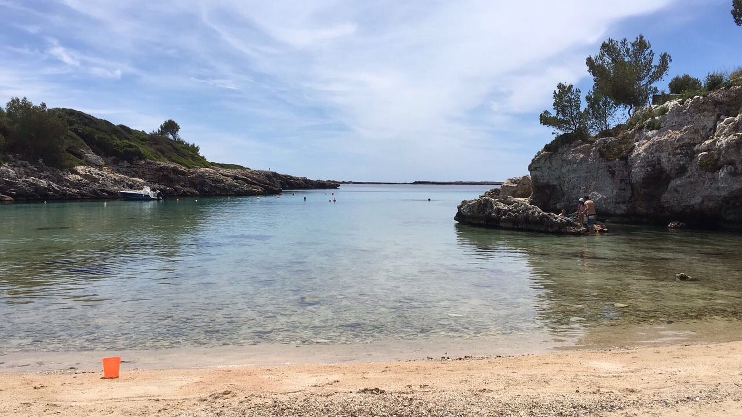 Ein Strand mit klarem Wasser, felsigem Ufer und spärlicher Vegetation.
