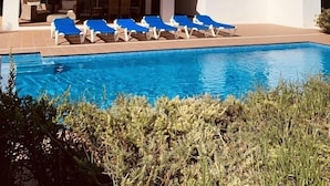 En vit byggnad med en swimmingpool, blå solstolar och en täckt uteplats.