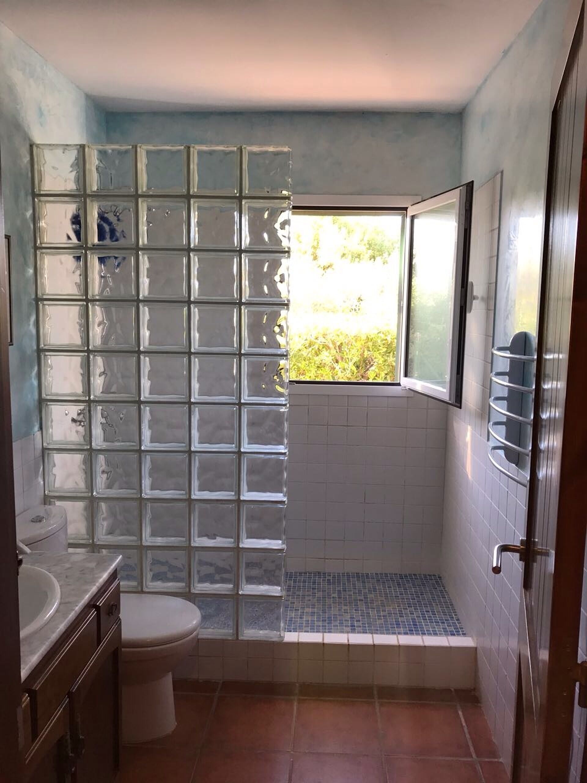A bathroom with a glass partition, a toilet, a sink, and a shower area.