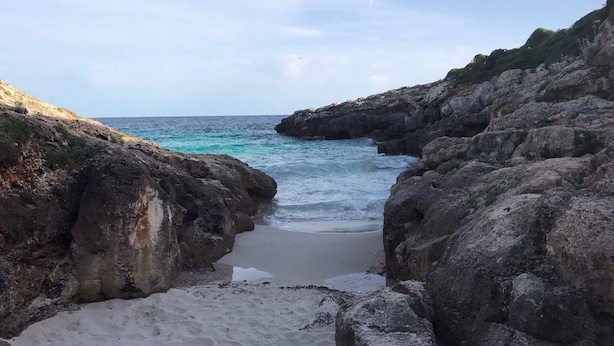 En klippig kuststräcka med en smal strand som leder ner till havet.