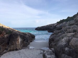 Eine felsige Küstenlinie mit einem schmalen Strand, der zum Meer führt.