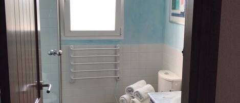 A bathroom with a toilet, a towel rack, a window, and a shower area.